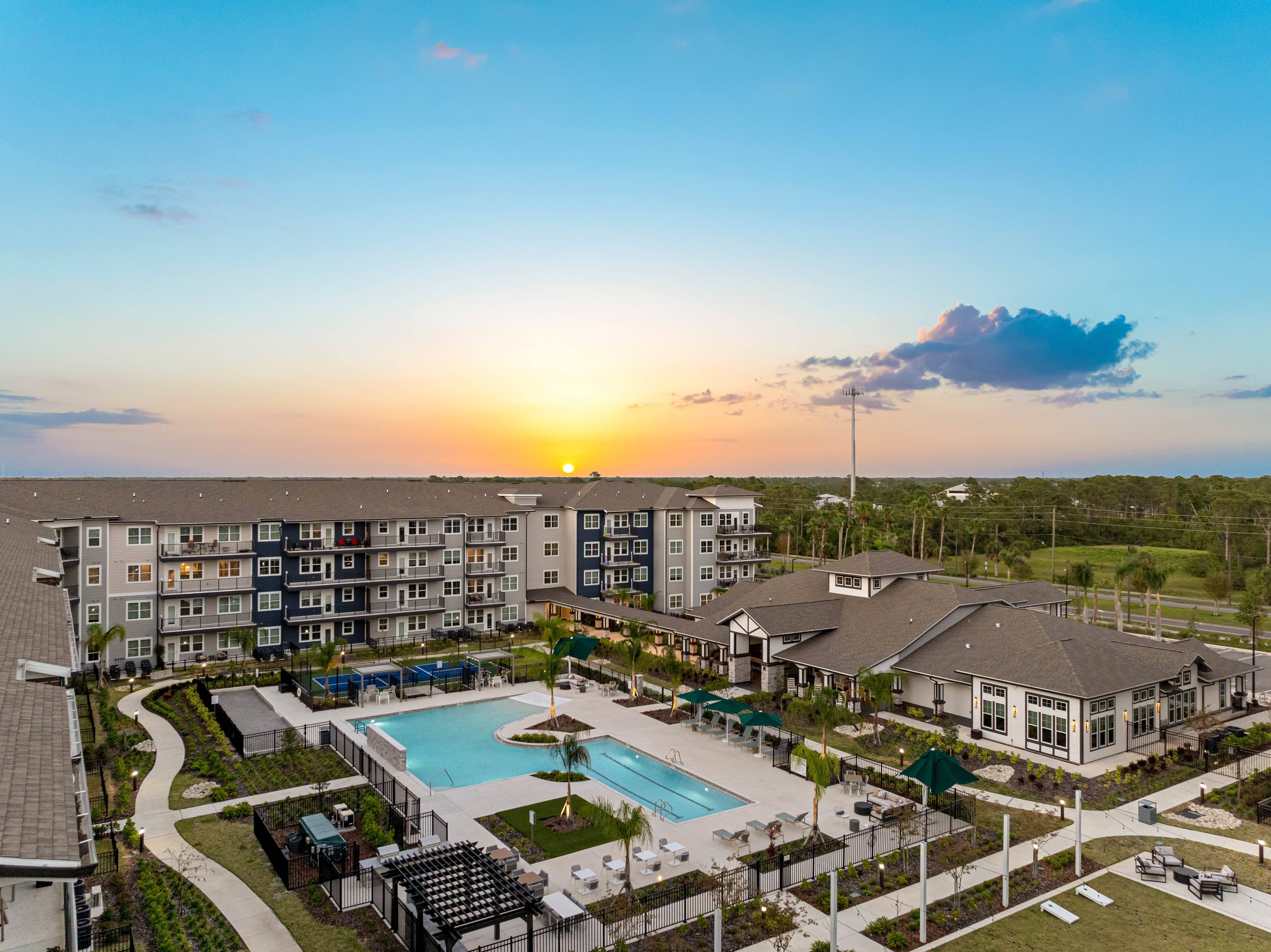 A sunset view of a resort with a pool and apartment buildings.